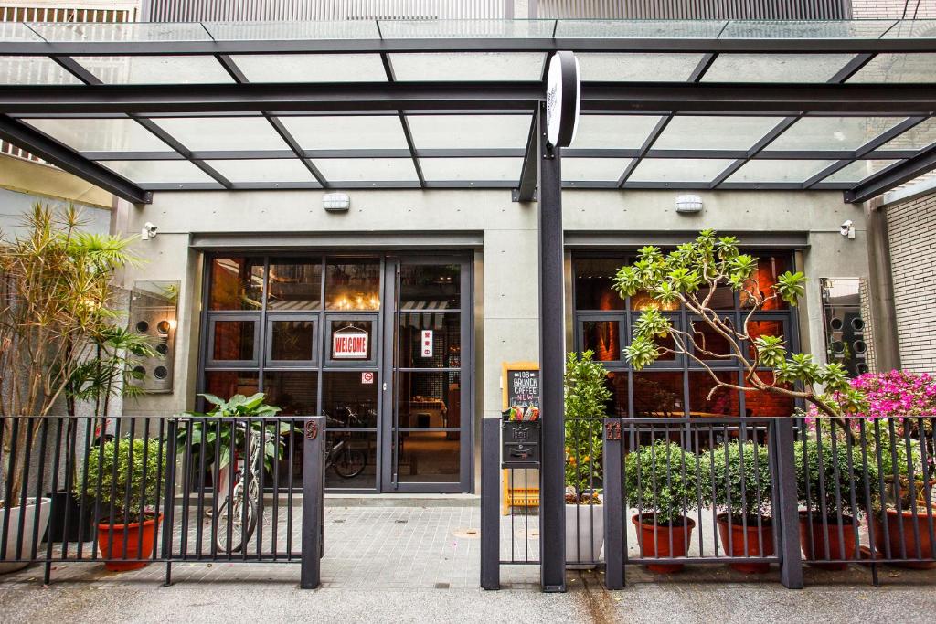 Cafe entrance with glass doors, black metal railing, and a glass canopy, surrounded by potted plants and a bike nearby