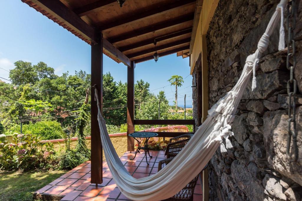 White fabric hammock tied between wooden posts on a stone-paved porch with a garden beyond.