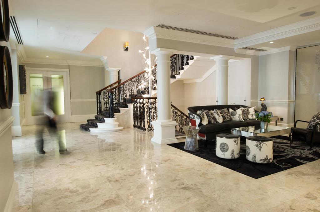 Luxurious hotel lobby with marble floor, white columns, ornate staircase railing, and a black sectional sofa with patterned cushions in a seating area.
