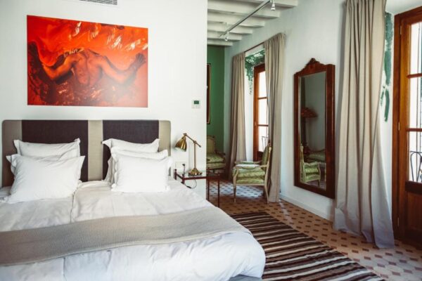 Hotel bedroom with a large bed, white linens, and a bold red painting above the headboard.