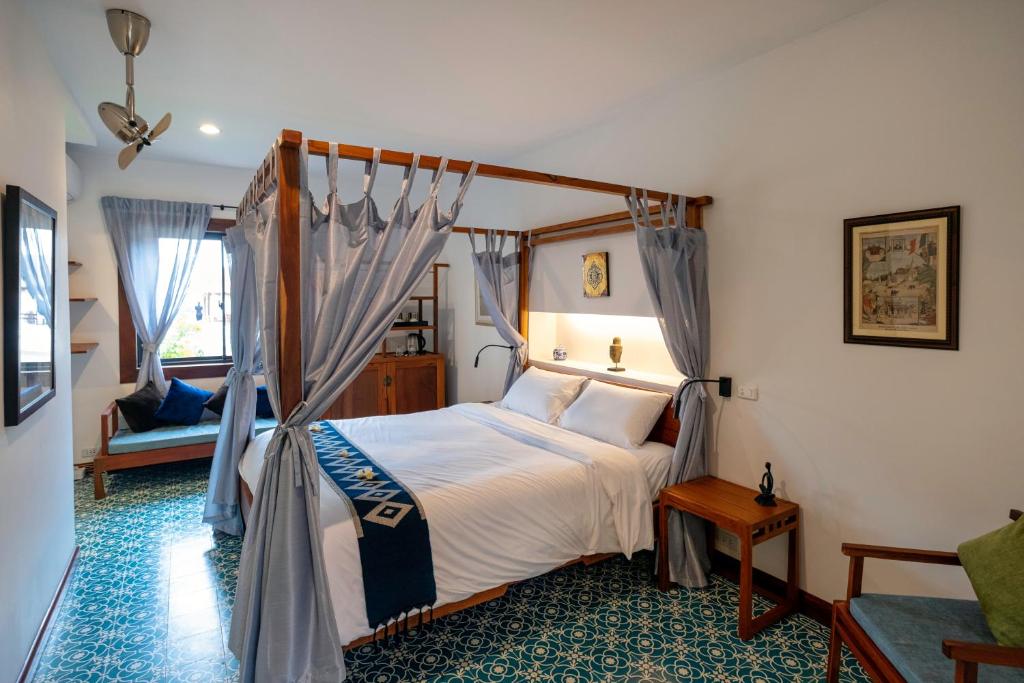 Four-poster bed with light blue curtains and white linens in a bright hotel room, teal patterned floor, and wooden side tables nearby.