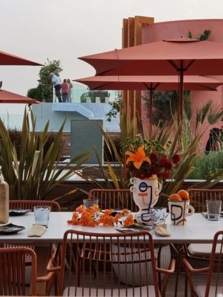 Rooftop restaurant with orange patio umbrellas, a long table set with flowers and place settings, and greenery around the space.