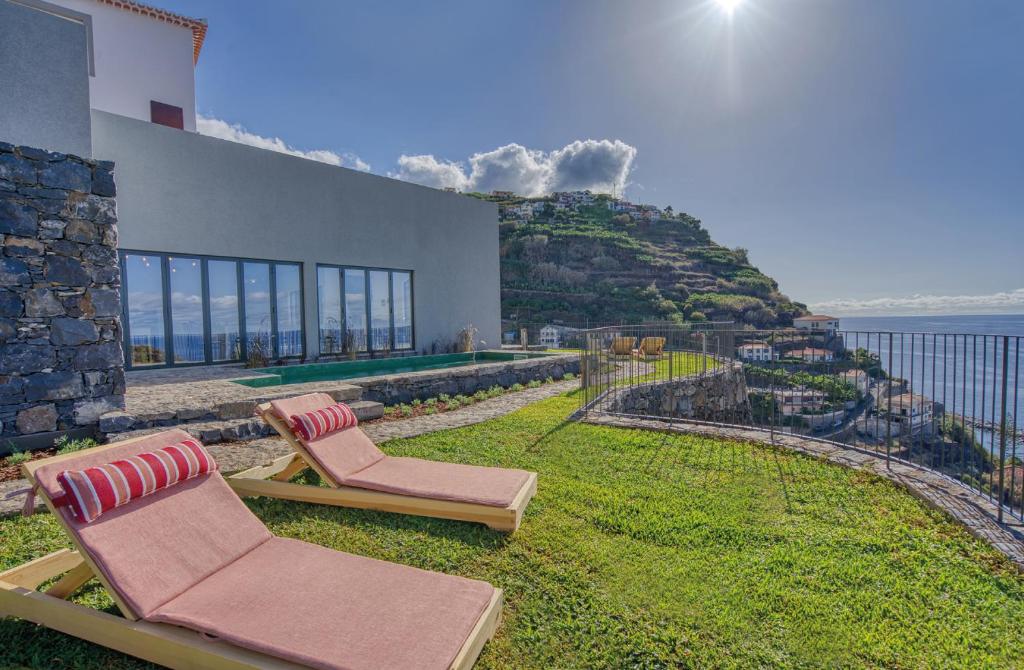 Two pink cushioned lounge chairs on a grassy terrace overlooking the sea and hillside village below.