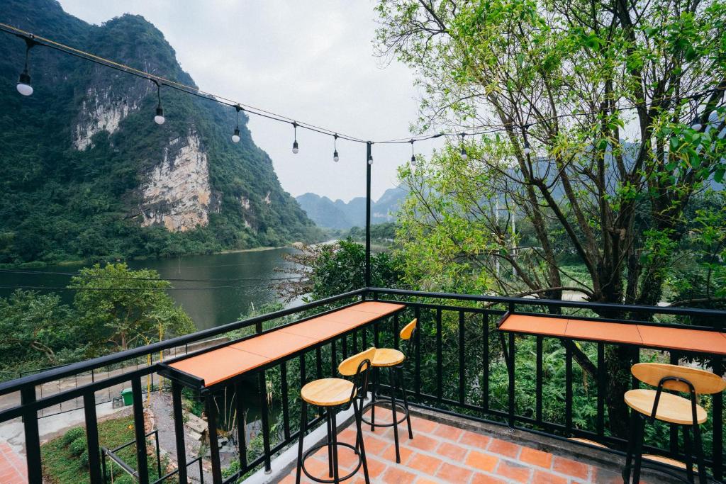 Al fresco cafe terrace with orange counter seating and high stools, overlooking a river and green, mountainous landscape with string lights above.