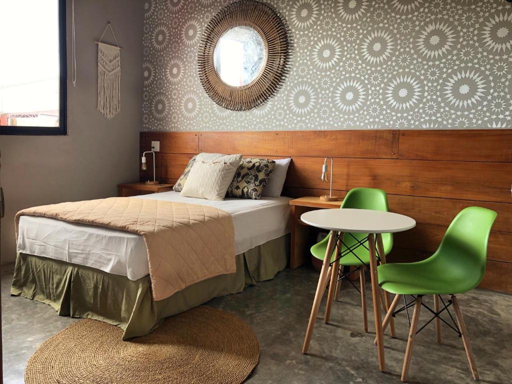Cozy bedroom with a queen bed, beige quilt, pillows, two green mid-century chairs, and a round white table.