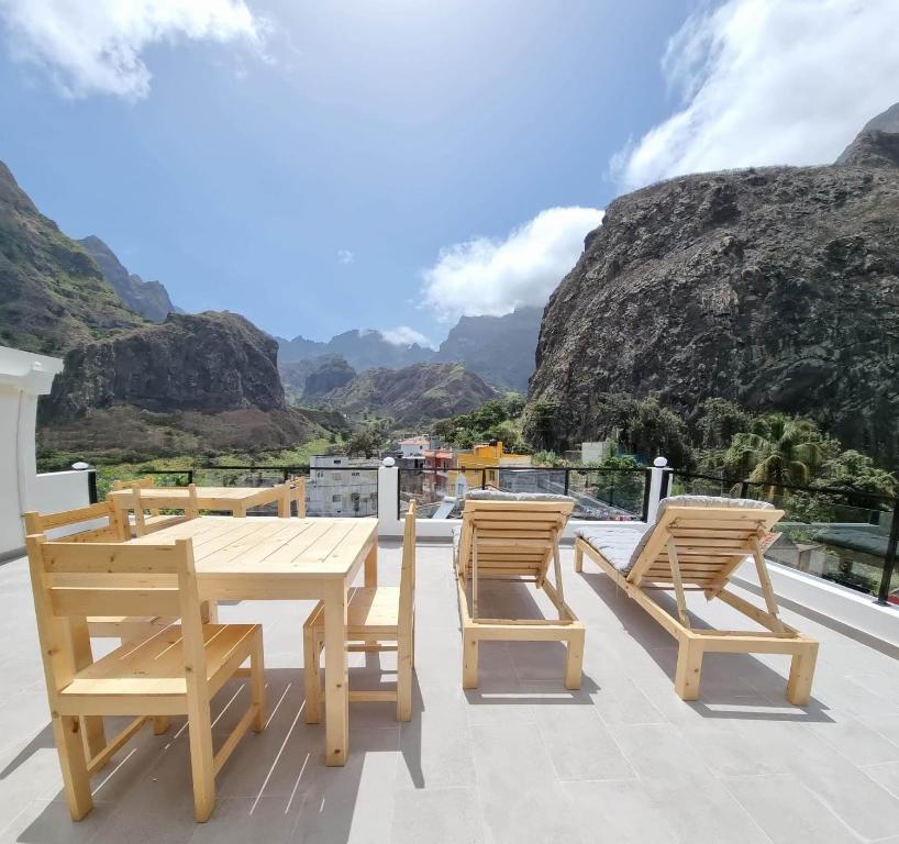 Terrace with a wooden table and chairs and two sun loungers, overlooking a valley with rocky mountains.
