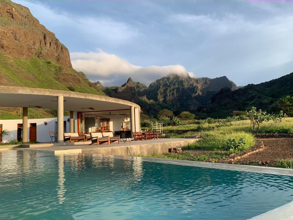 Poolside pavilion with curved roof and lounge chairs, beside a rectangular pool with green mountains in the background.