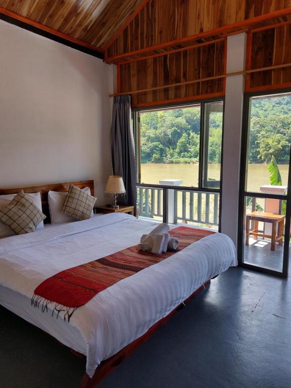 Rustic bedroom with a large bed, white linens, plaid pillows, wooden ceiling, and a balcony view of a lake and trees outside.