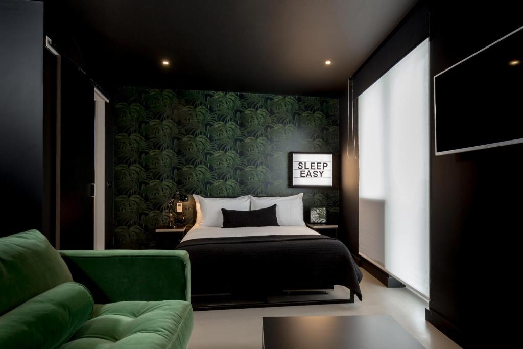 Hotel bedroom with a dark tropical wallpaper accent wall, a neatly made bed, and a green velvet sofa in the foreground.