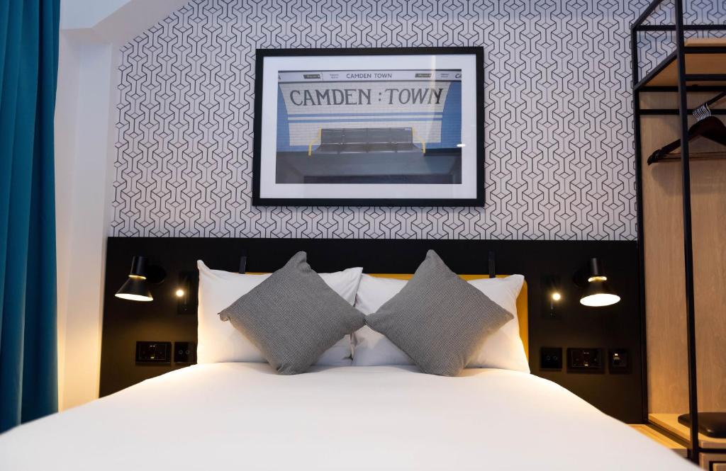 Hotel bedroom with a bed, two gray pillows, and a framed Camden Town artwork above the headboard.