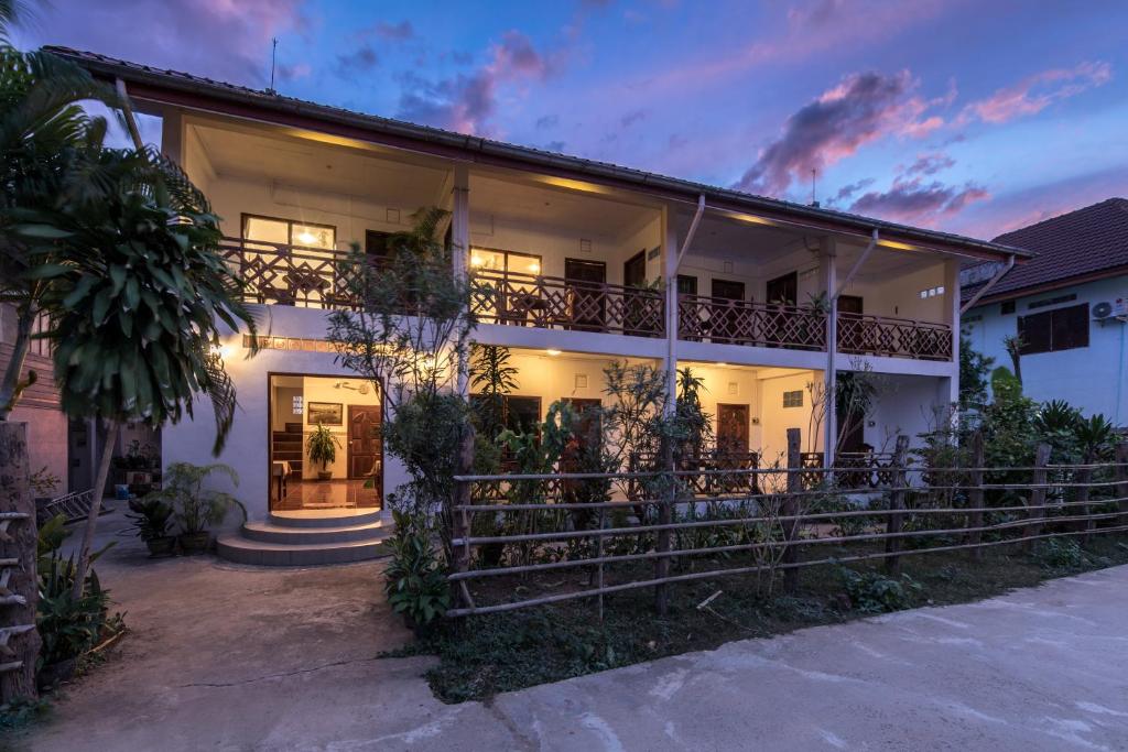 Two-story guesthouse with a lit entrance, balconies, and tropical plants at dusk.