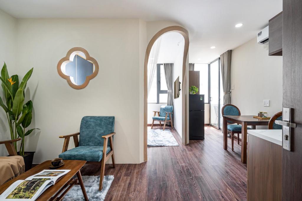 Modern living area with turquoise chairs, wood floor, and plants; arched doorway leads to a small dining/kitchen area with a fridge and table.