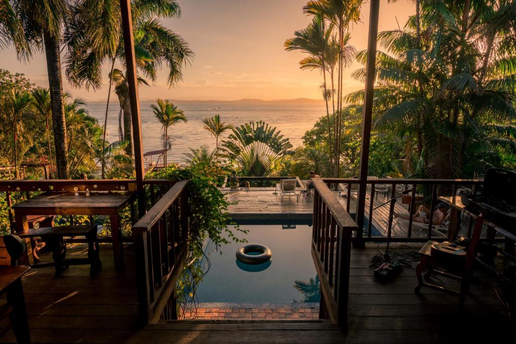 Tropical deck with a small pool overlooking a sunset-lit ocean, surrounded by palm trees and lounge chairs on the deck.