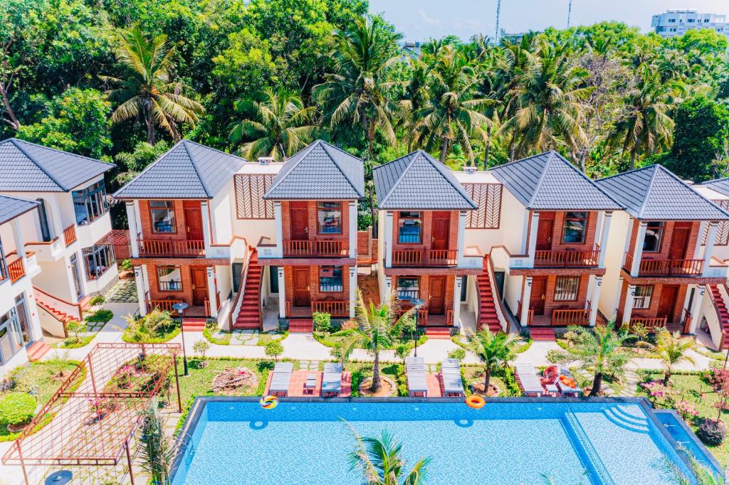 Row of two-story villas with red doors and grey roofs surrounding a large pool area with palm trees and lounge chairs.