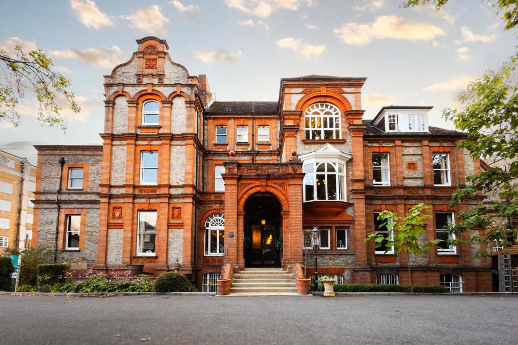 Historic red-brick building with an ornate arched entrance and large bay windows, front steps framed by planters and greenery.