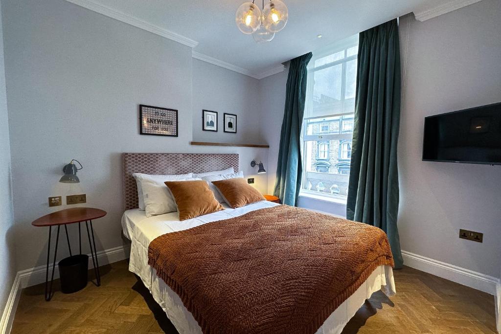 Hotel bedroom with a queen bed, brown bedspread, two orange-brown pillows, gray headboard, and side tables with lamps.