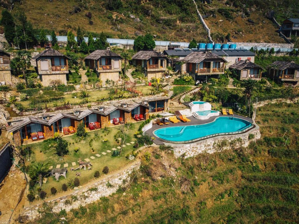 H hillside: rustic wooden cabins lining a terraced hillside around a curved blue swimming pool with loungers and sun umbrellas.