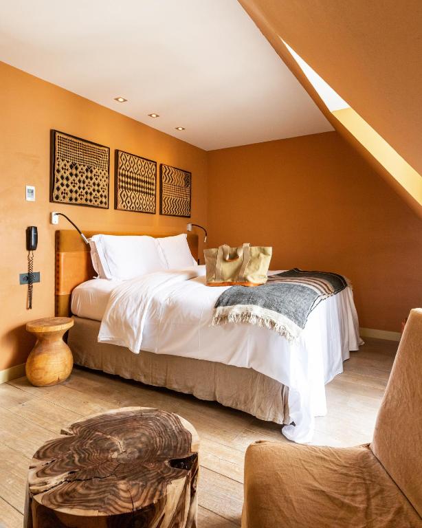 Cozy hotel bedroom with white bedding, orange walls, and geometric wall art above the bed under a slanted ceiling.