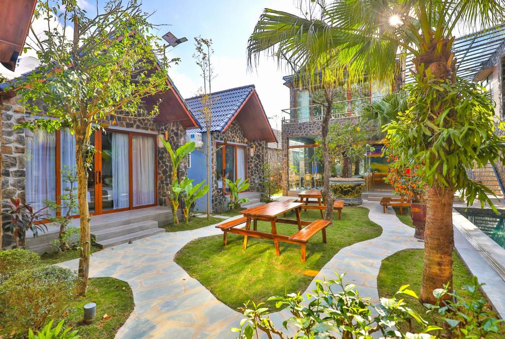 Courtyard of a tropical resort with stone cottages, wooden doors, green lawn, and wooden picnic tables far side of the garden.