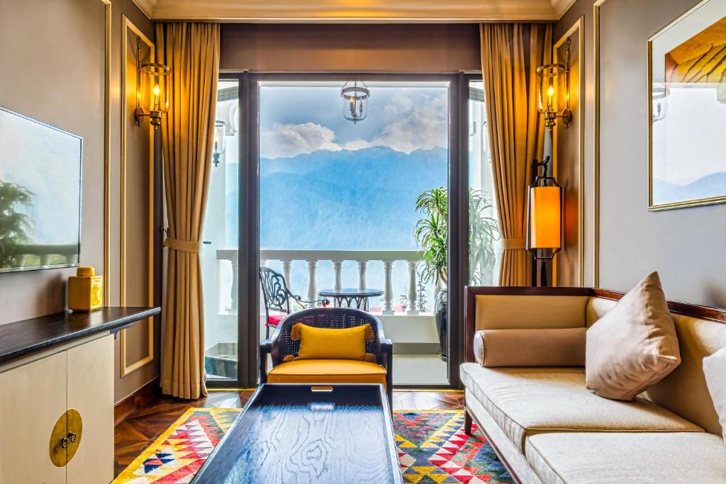 Luxurious hotel living room with cream sofa, colorful rug, and glass doors leading to a balcony overlooking blue mountains.