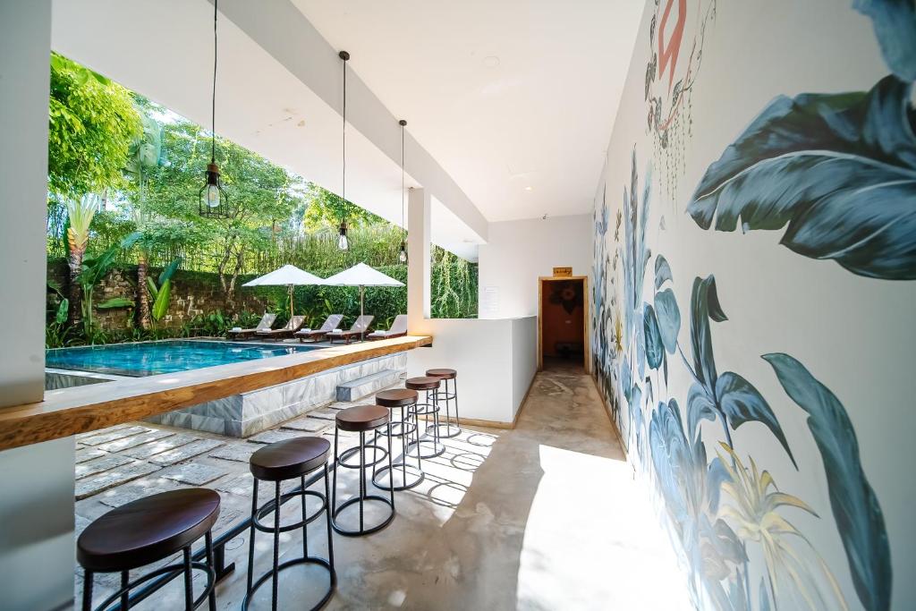 Bar counter with brown stools beside a glass wall overlooking a pool area with lounge chairs and umbrellas; a tropical mural runs along the right wall.