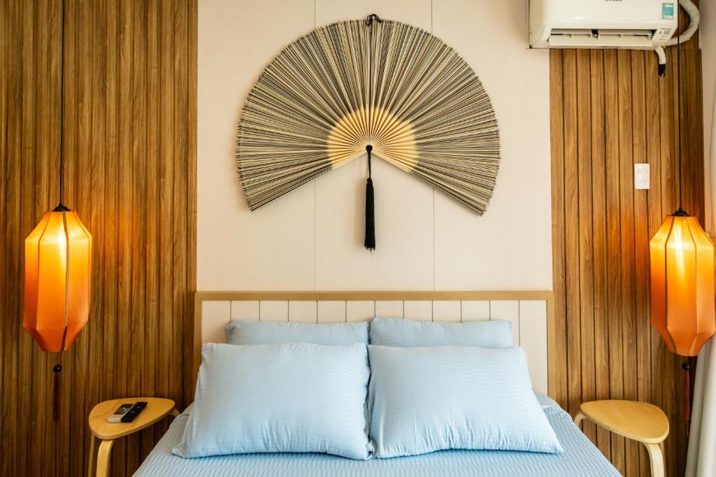 Bedroom with a large fan-shaped wall art above a white bed and pale blue pillows, flanked by orange lantern lamps on wood-paneled walls.