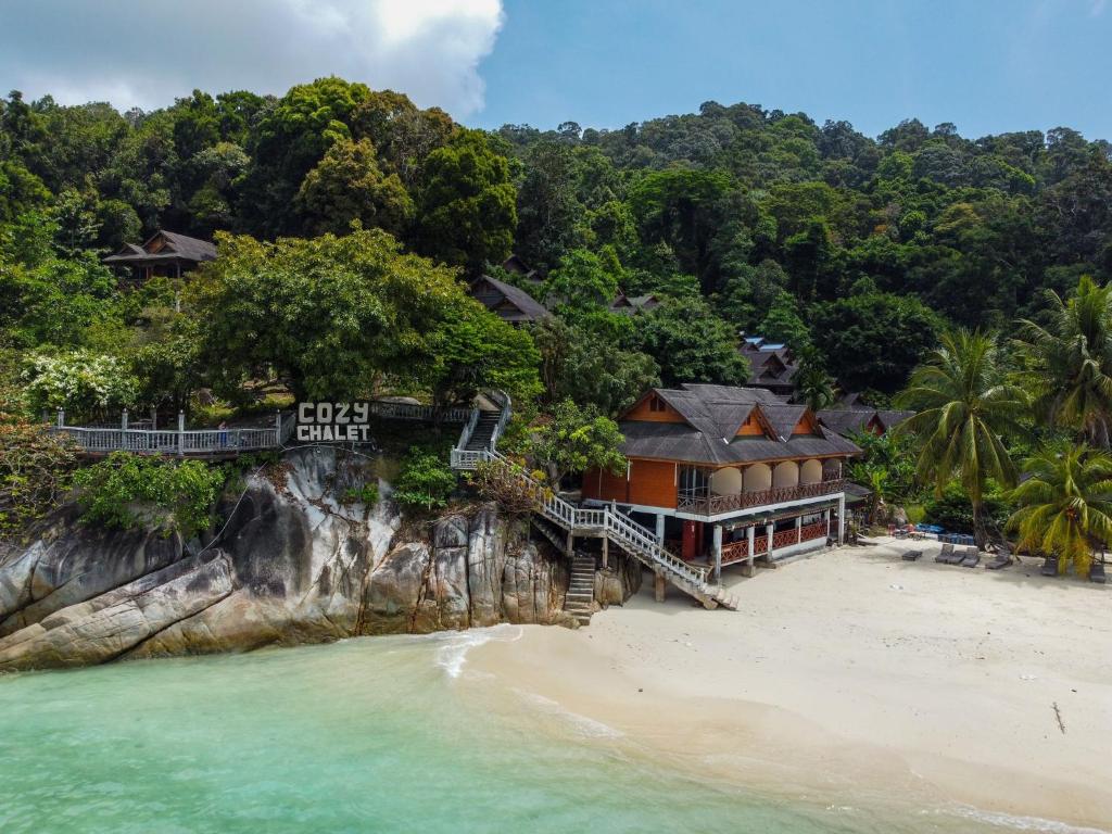 Cozy chalet resort built on a rocky cliff overlooking a white-sand beach and turquoise sea, surrounded by palm trees and forest.
