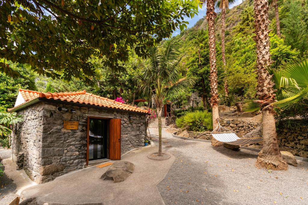 Stone cottage with orange-tiled roof in a tropical garden, a hammock hung between palm trees.