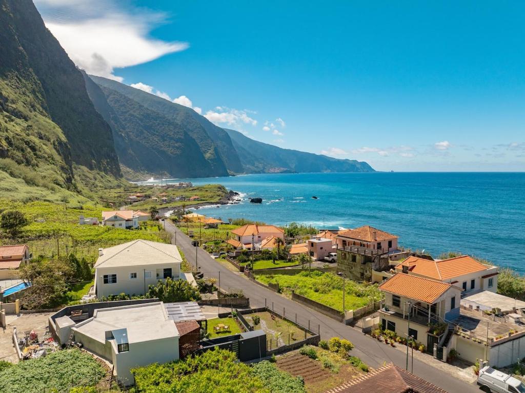 A coastal hillside village with orange-tiled houses, a winding street, and towering cliffs meeting the blue ocean under a clear sky.