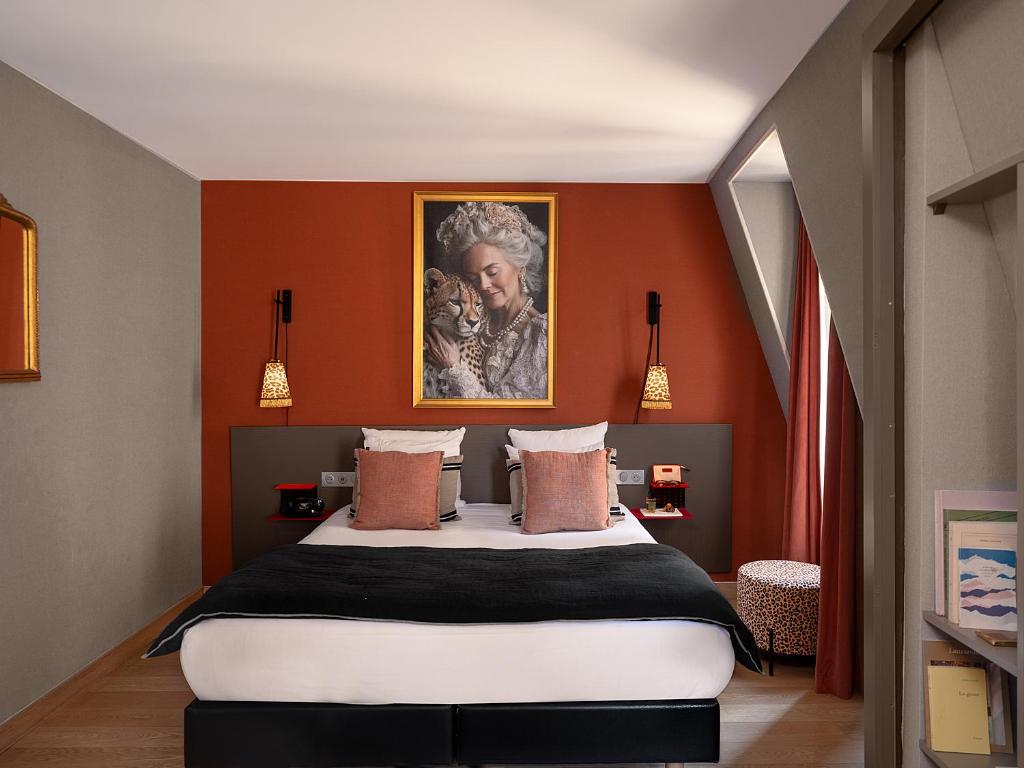 Hotel bedroom with a large bed, coral accent wall, and a framed portrait above the headboard.