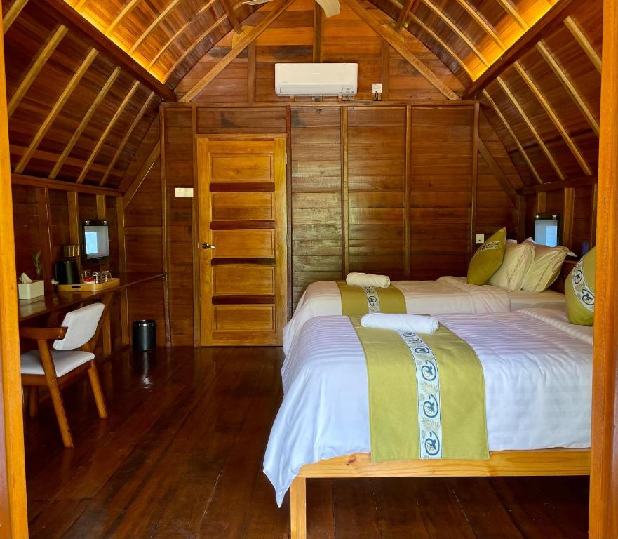 Wood-paneled attic hotel room with two white beds, green runners, rolled towels, and an air conditioner on the wall above the door.