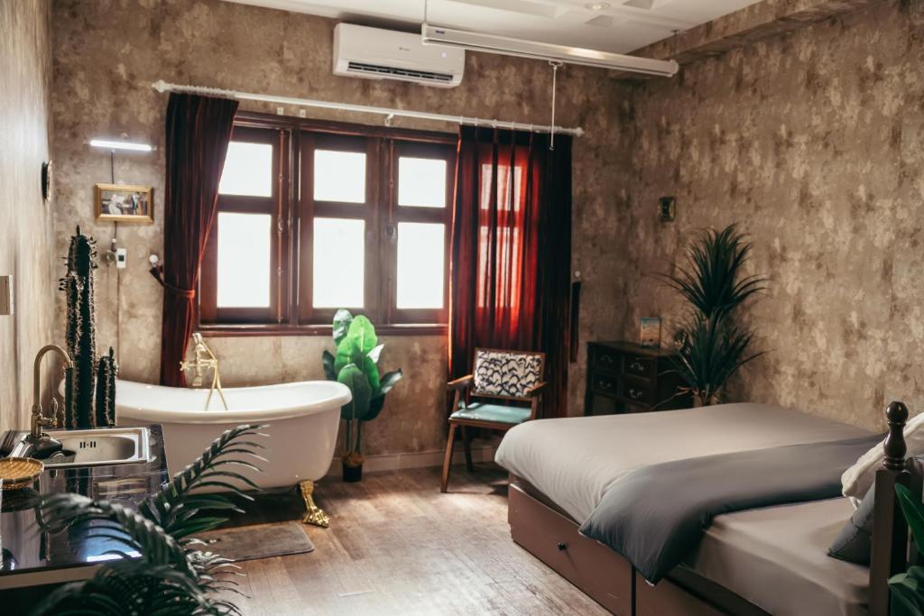 Rustic bedroom with a white freestanding clawfoot tub by a large window, a gray-bedding bed, and green plants.