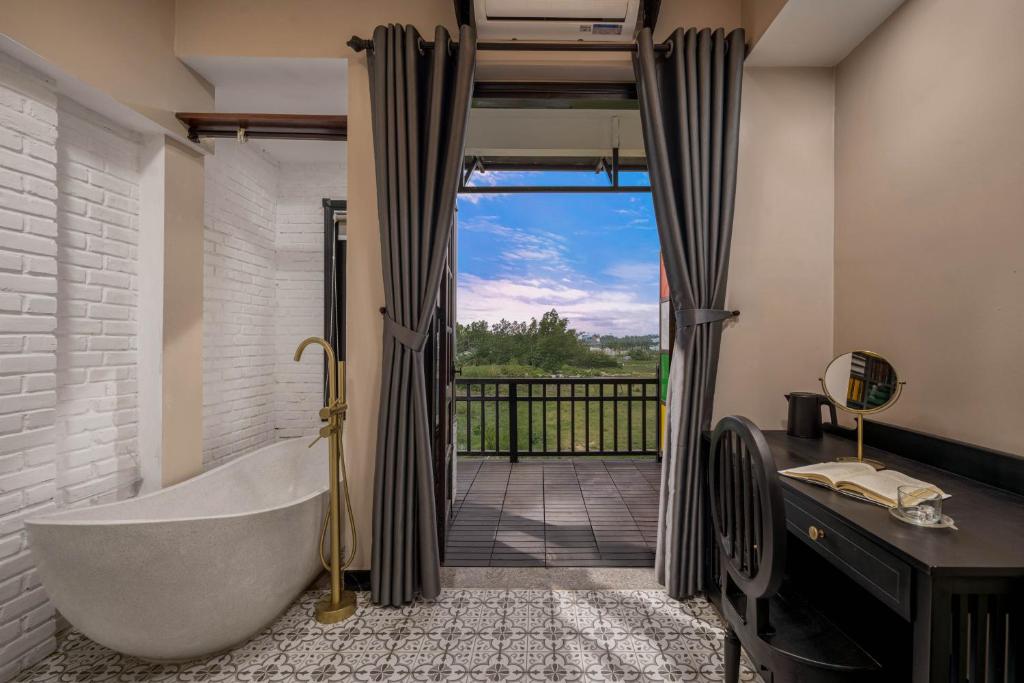 Stylish bathroom with a freestanding oval tub and gold faucet on the left, white brick wall and patterned tile, opening onto a balcony with a green landscape beyond.