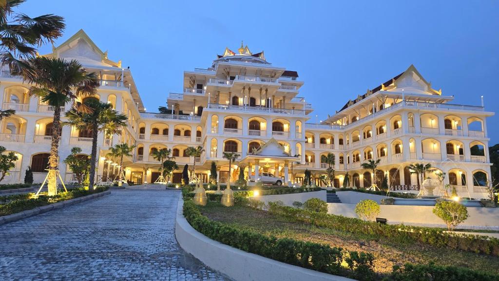 Grand white luxury hotel complex in laos with palm trees and arched balconies, illuminated at dusk along a stone driveway.