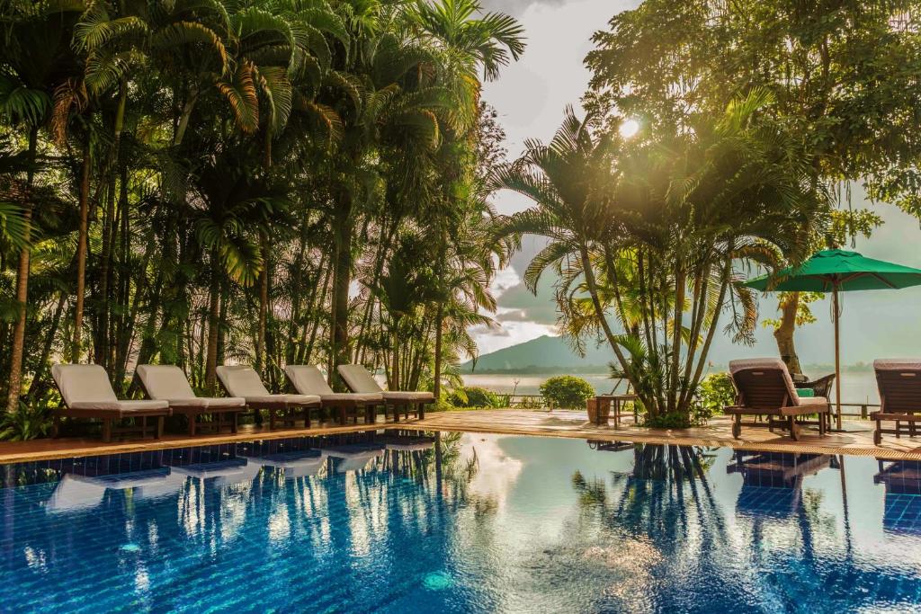 Poolside view with row of white lounge chairs, palm trees, and a reflecting blue pool at sunset by a tropical resort