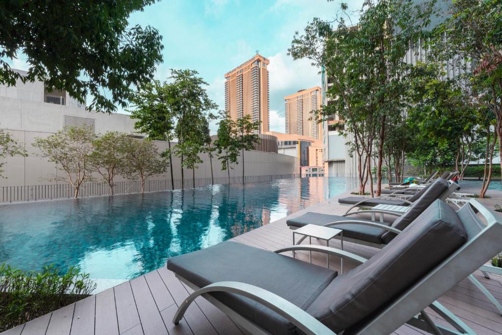 Rooftop outdoor pool with lounge chairs along the edge, trees, and a city skyline in the distance.