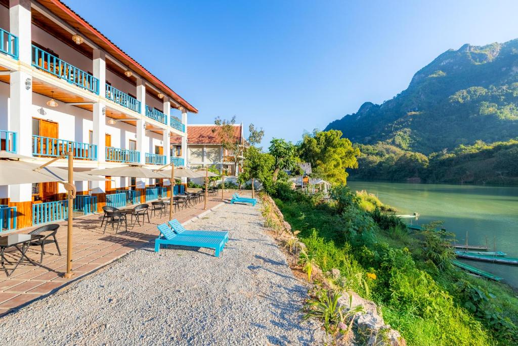 Coastal resort with white building, blue balconies, outdoor seating, and a lake with green mountains in the background