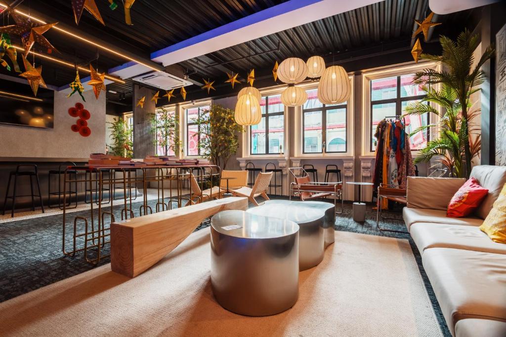 Modern lounge/bar interior with a long high table, metal stools, and round metallic ottomans under warm hanging lanterns and festive stars.