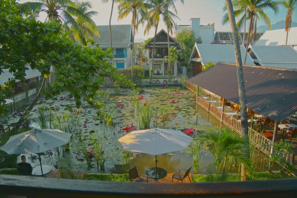 Resort courtyard with a pond filled with lily pads, patio tables with umbrellas, and palm trees surrounding bungalows.