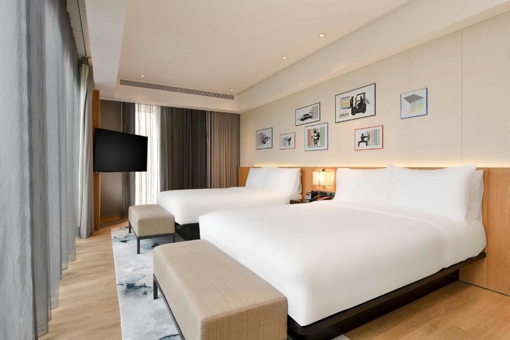 Hotel room with two large beds, white linens, beige benches, and a row of framed art above the headboards.