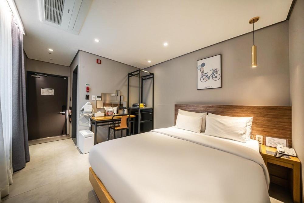 Hotel room with a large bed, wooden headboard, and a work desk area near the entry left side.