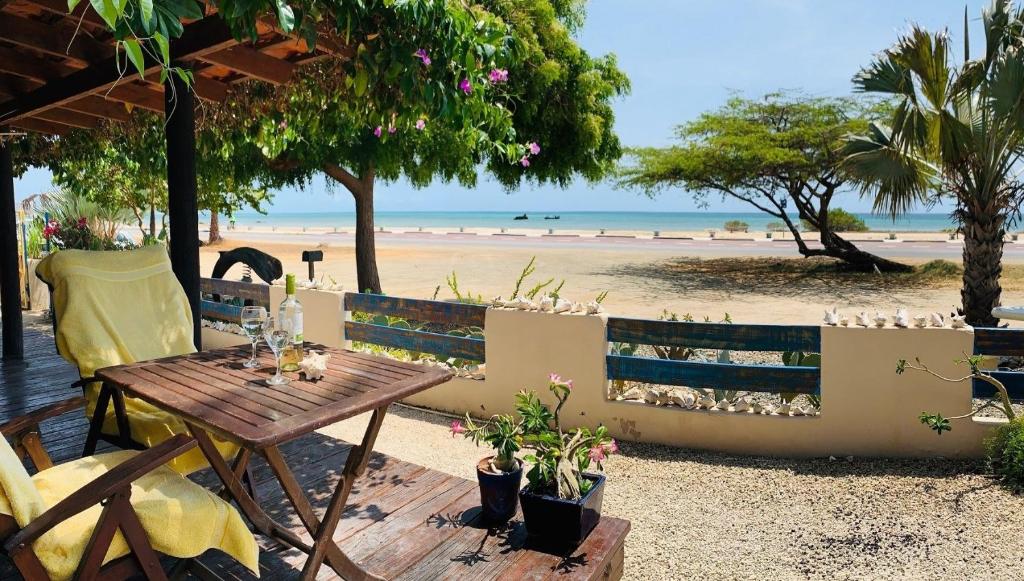 Beachfront patio with a small table set for two, wine bottle and glasses, yellow chairs, facing a sandy beach and calm sea.