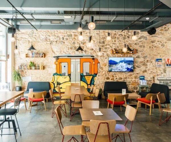 Cafe interior with stone wall, orange bus mural, wooden tables and chairs, and pendant lighting.