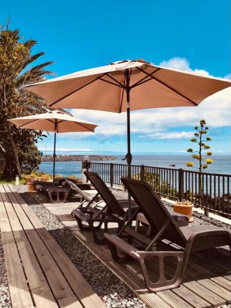 Seaside deck with tan umbrellas and lounge chairs facing the ocean.