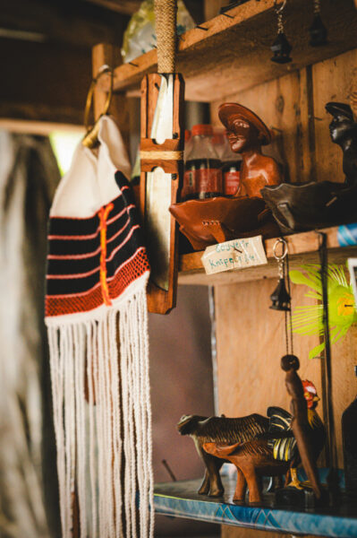 Wooden shelf with carved animal figurines, woven textile hanging nearby, and small souvenirs on display.