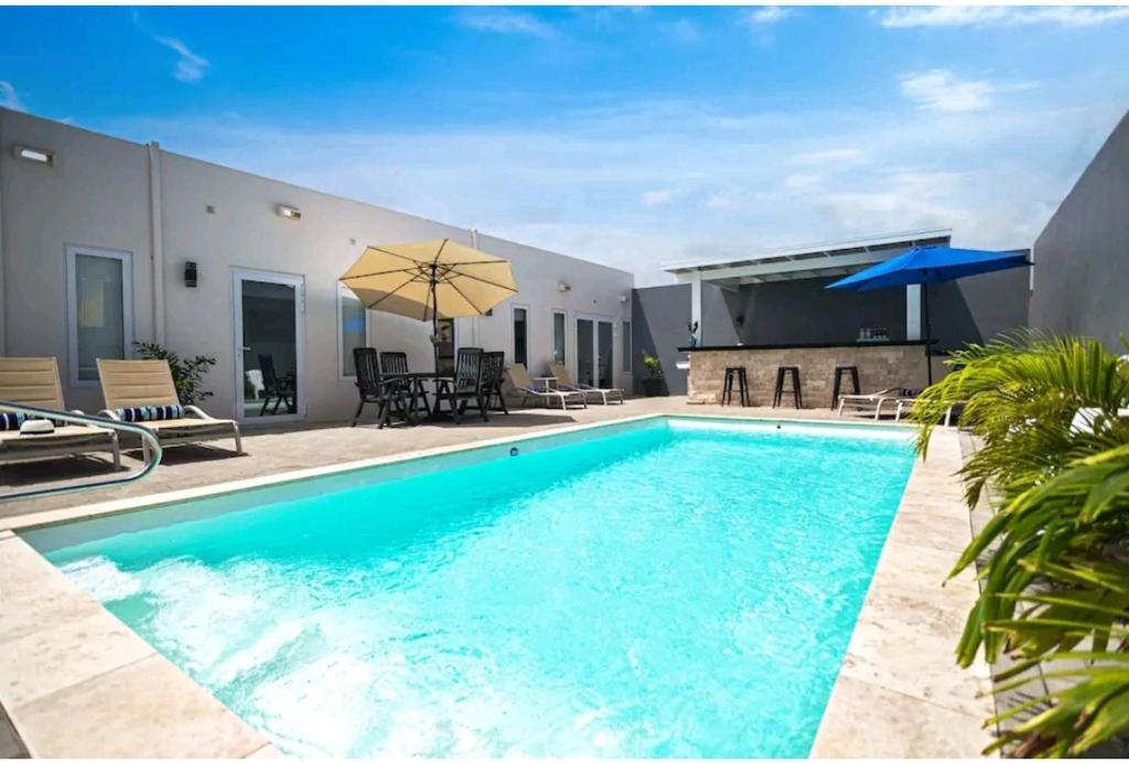 Sunny poolside lounge area with turquoise pool, beige loungers, and patio dining near a bar under a blue sky.