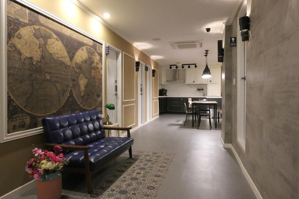 Hallway seating area with a blue tufted sofa beside a large world map mural and a potted flowers near the wall, leading to a kitchen/dining area in back.