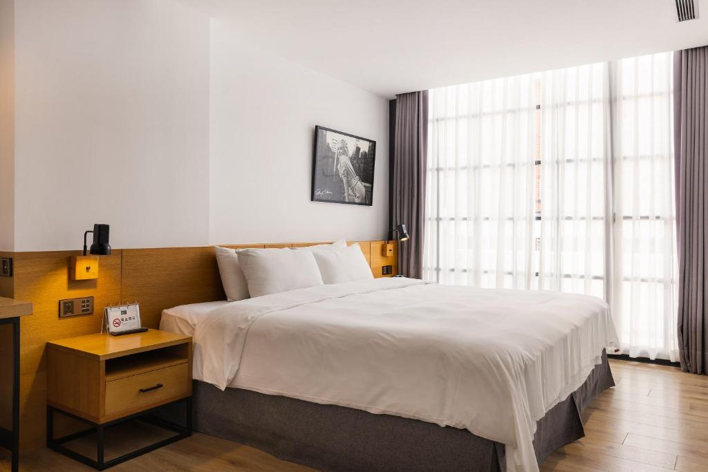 Modern hotel room with a king-size bed, white linens, two wooden nightstands, and large windows with sheer curtains.