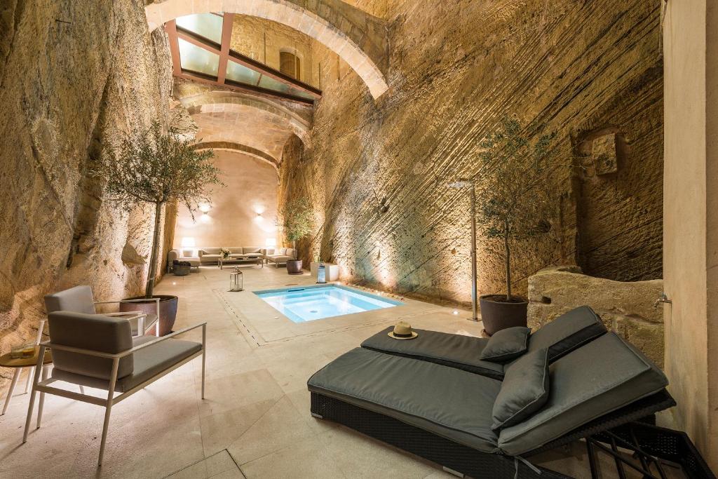 Luxurious indoor pool area built into a rock cavern with seating, loungers, and potted plants with warm lighting.