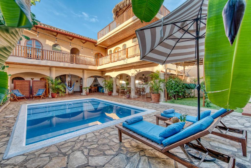 Courtyard with a rectangular pool, blue lounge chairs, and a striped umbrella under clear blue sky.